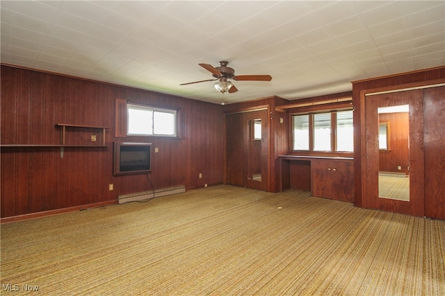 unfurnished living room featuring light colored carpet, baseboard heating, wooden walls, and ceiling fan