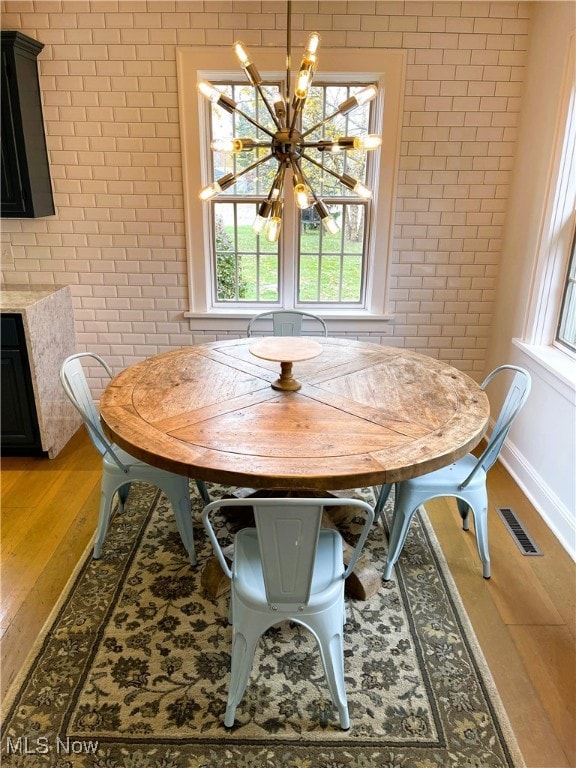 dining room with hardwood / wood-style flooring, an inviting chandelier, and brick wall