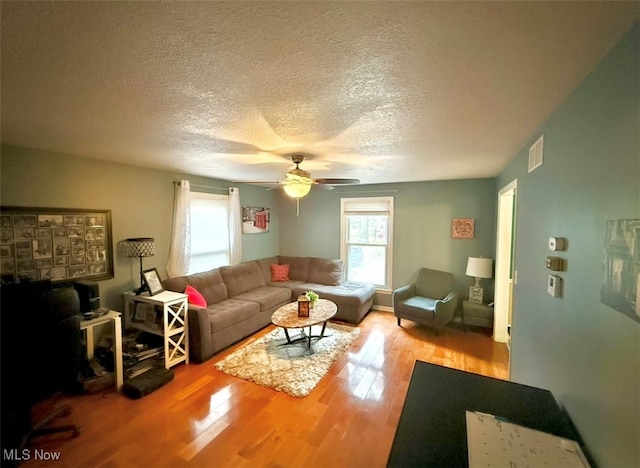 living room featuring a textured ceiling, light wood-type flooring, and ceiling fan