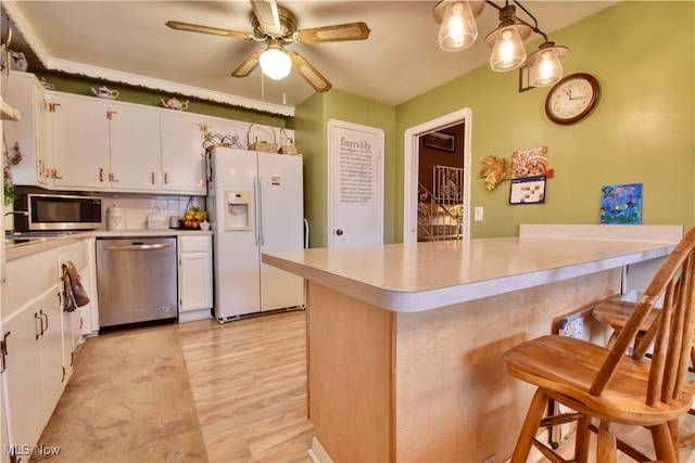 kitchen with white cabinetry, hanging light fixtures, light hardwood / wood-style flooring, a breakfast bar area, and appliances with stainless steel finishes