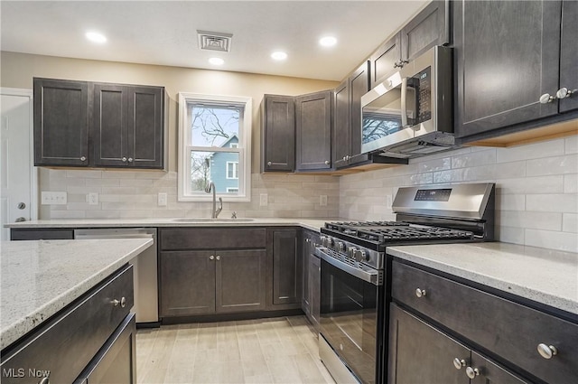 kitchen featuring light stone countertops, sink, stainless steel appliances, decorative backsplash, and dark brown cabinets