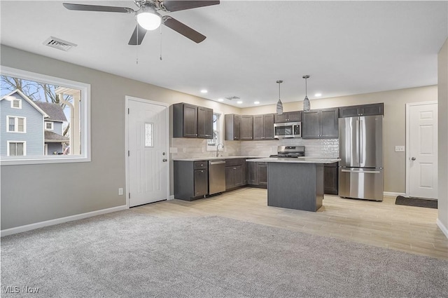 kitchen with ceiling fan, backsplash, decorative light fixtures, a kitchen island, and appliances with stainless steel finishes