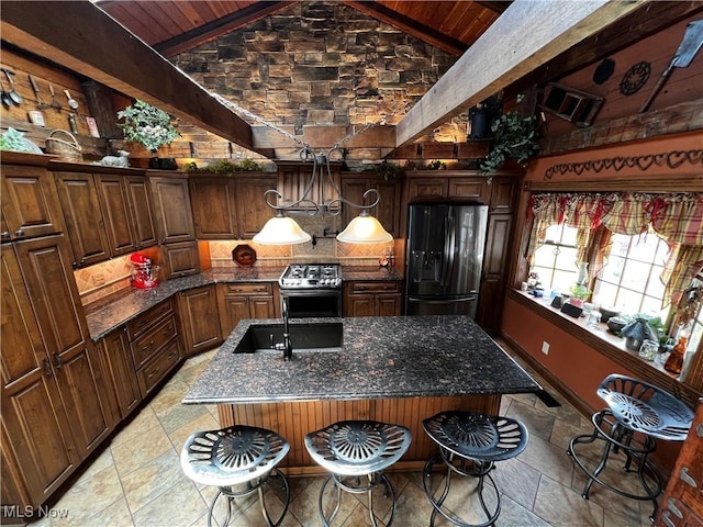 kitchen featuring a kitchen island with sink, stainless steel range oven, dark stone countertops, and fridge with ice dispenser