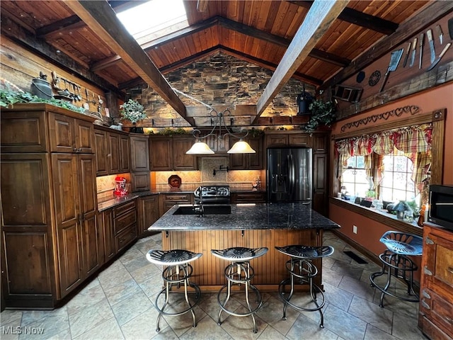 kitchen featuring black appliances, wood ceiling, vaulted ceiling with beams, an island with sink, and a kitchen breakfast bar