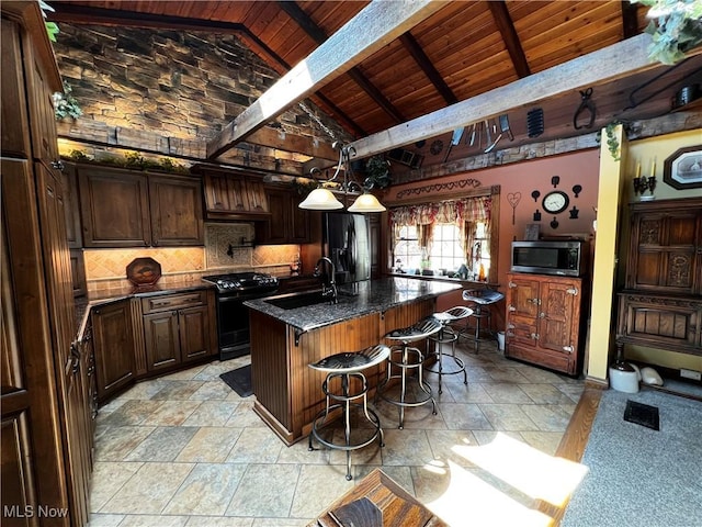 kitchen with black appliances, an island with sink, vaulted ceiling with beams, wooden ceiling, and a breakfast bar area