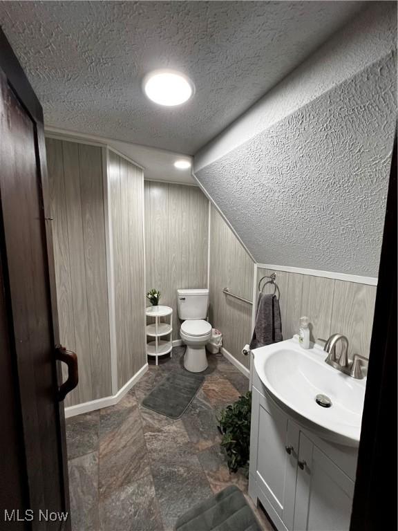 bathroom featuring toilet, wood walls, lofted ceiling, a textured ceiling, and vanity