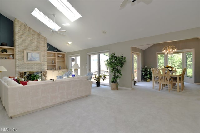 carpeted living room with ceiling fan with notable chandelier, high vaulted ceiling, a skylight, and a fireplace