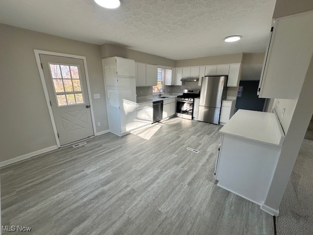 kitchen featuring a textured ceiling, white cabinets, stainless steel appliances, and light hardwood / wood-style floors