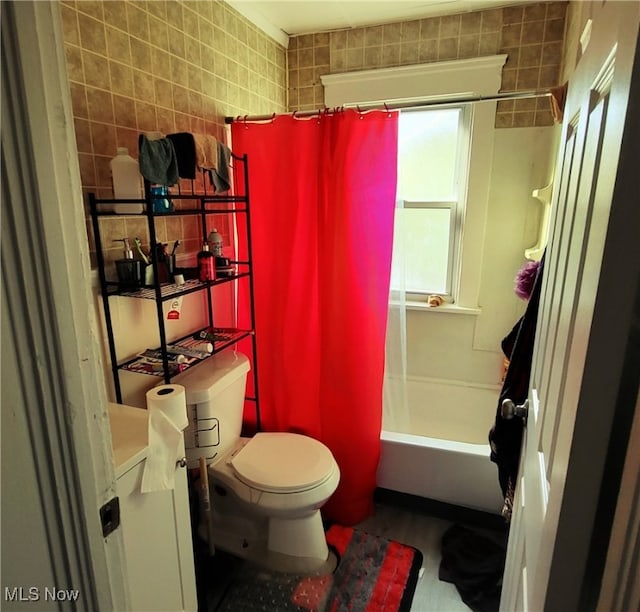 bathroom with tile walls, toilet, and shower / bathtub combination with curtain