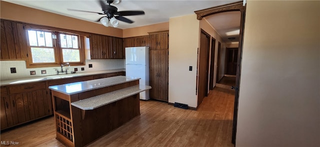 kitchen featuring sink, a center island, decorative backsplash, light hardwood / wood-style flooring, and white refrigerator