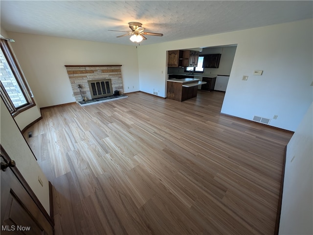 unfurnished living room featuring a fireplace, a textured ceiling, light wood-type flooring, and ceiling fan