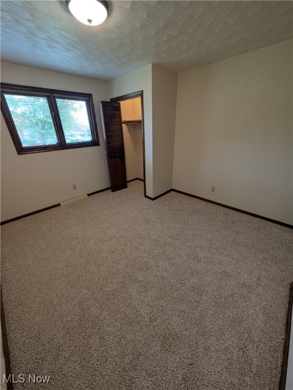 unfurnished bedroom featuring a walk in closet, a textured ceiling, a closet, and carpet floors