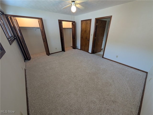 unfurnished bedroom featuring multiple closets, light colored carpet, and ceiling fan