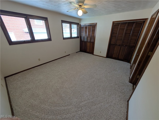 unfurnished bedroom featuring a textured ceiling, two closets, carpet flooring, and ceiling fan