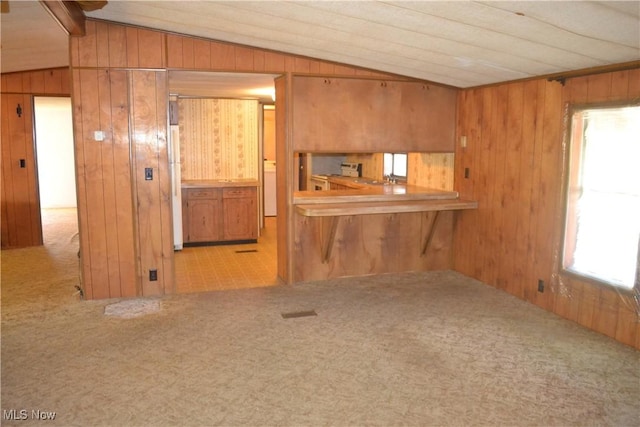 kitchen with lofted ceiling, kitchen peninsula, wood walls, and white fridge