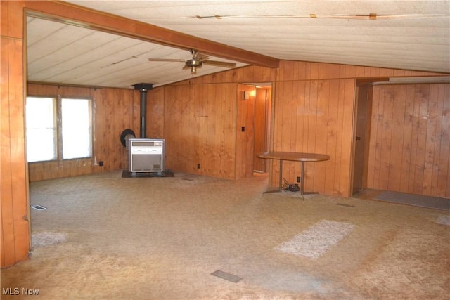 unfurnished living room featuring ceiling fan, wooden walls, lofted ceiling with beams, and a wood stove