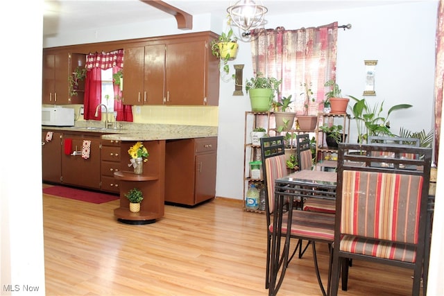 kitchen featuring backsplash, sink, pendant lighting, a chandelier, and light hardwood / wood-style floors