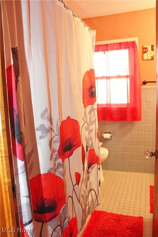 bathroom with toilet and tile walls