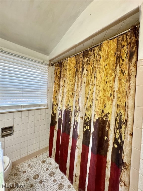 bathroom with tile patterned flooring, toilet, lofted ceiling, and tile walls