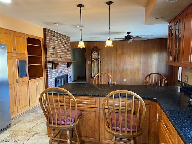 kitchen with ceiling fan, decorative light fixtures, a fireplace, stainless steel fridge, and wooden walls