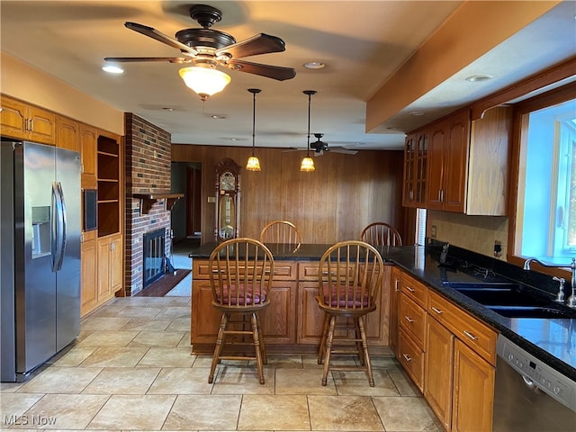 kitchen with a kitchen bar, wooden walls, sink, pendant lighting, and appliances with stainless steel finishes