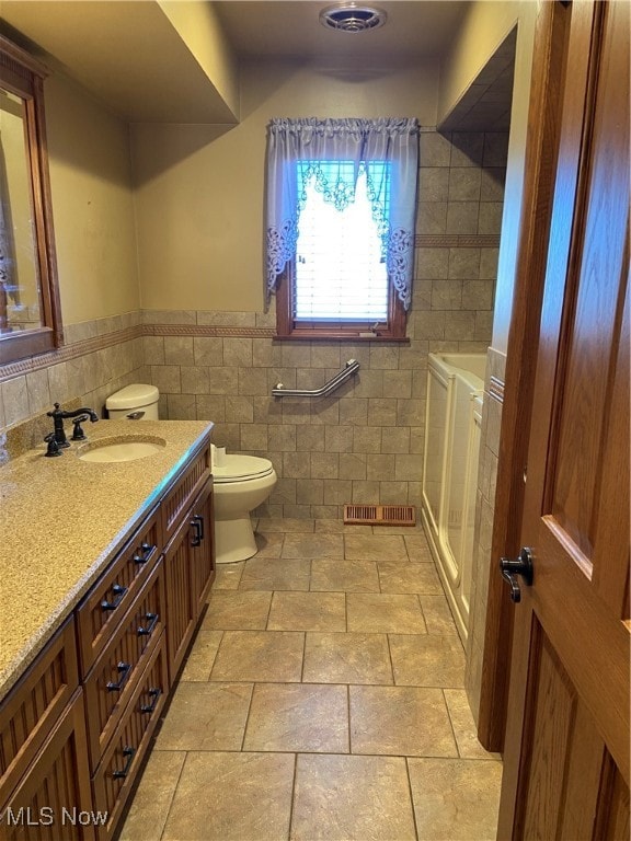 bathroom featuring toilet, vanity, and tile walls