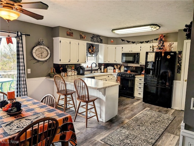 kitchen featuring white cabinetry, a breakfast bar, black appliances, kitchen peninsula, and dark wood-type flooring