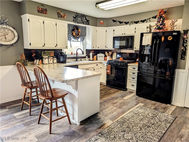 kitchen featuring kitchen peninsula, black appliances, sink, dark hardwood / wood-style floors, and a breakfast bar