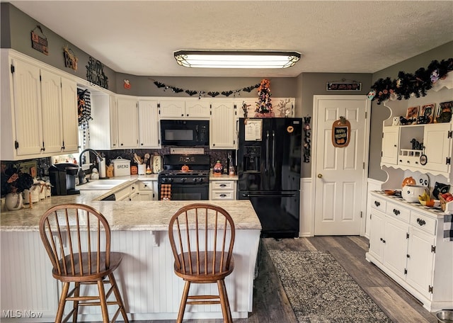 kitchen with black appliances, dark hardwood / wood-style floors, sink, a breakfast bar area, and kitchen peninsula