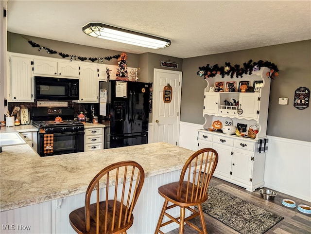 kitchen with black appliances, white cabinetry, dark hardwood / wood-style floors, a breakfast bar, and kitchen peninsula