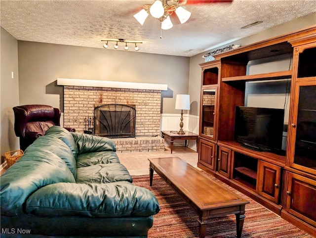 living room with a brick fireplace, a textured ceiling, and ceiling fan