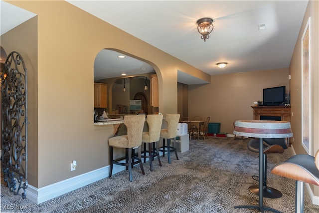 interior space featuring arched walkways, carpet, a breakfast bar area, light countertops, and baseboards