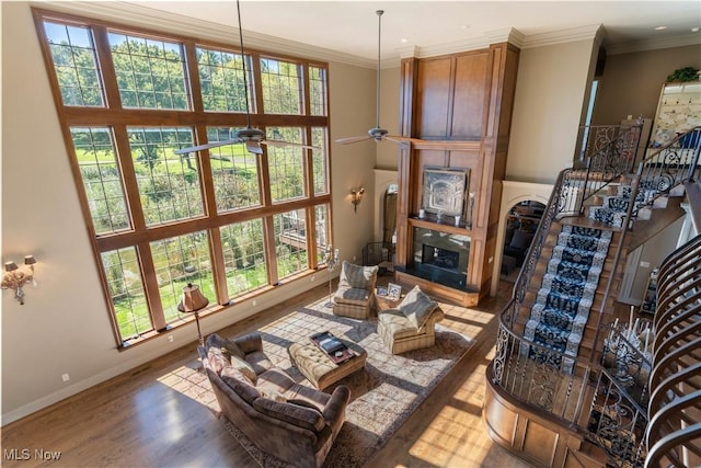 living room with a glass covered fireplace, stairs, crown molding, and wood finished floors