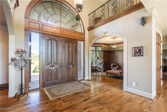 entrance foyer featuring wood-type flooring, a towering ceiling, and ornamental molding