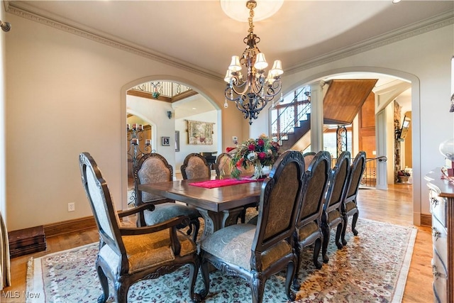 dining room featuring arched walkways, an inviting chandelier, crown molding, light wood finished floors, and baseboards