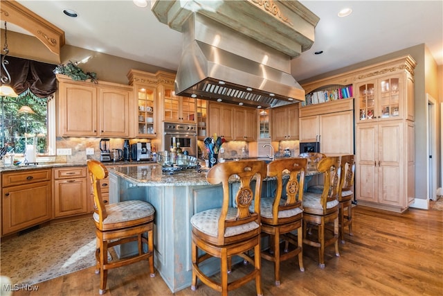 kitchen with light stone counters, island range hood, a kitchen island, hardwood / wood-style floors, and oven