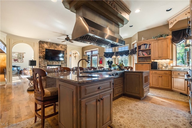 kitchen with sink, a kitchen island with sink, light hardwood / wood-style floors, a kitchen bar, and island range hood