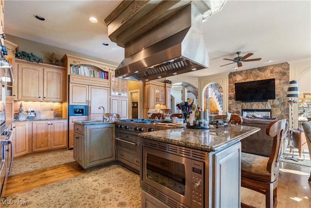 kitchen featuring ceiling fan, island exhaust hood, an island with sink, and light hardwood / wood-style flooring