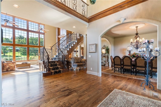 foyer with hardwood / wood-style floors, ceiling fan with notable chandelier, crown molding, and a high ceiling