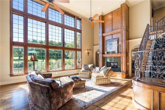 living area with baseboards, a tile fireplace, a high ceiling, wood finished floors, and a ceiling fan