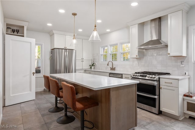 kitchen featuring a healthy amount of sunlight, stainless steel appliances, wall chimney exhaust hood, and a kitchen island