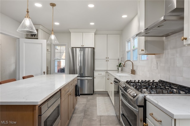 kitchen with wall chimney range hood, appliances with stainless steel finishes, sink, white cabinets, and light stone counters