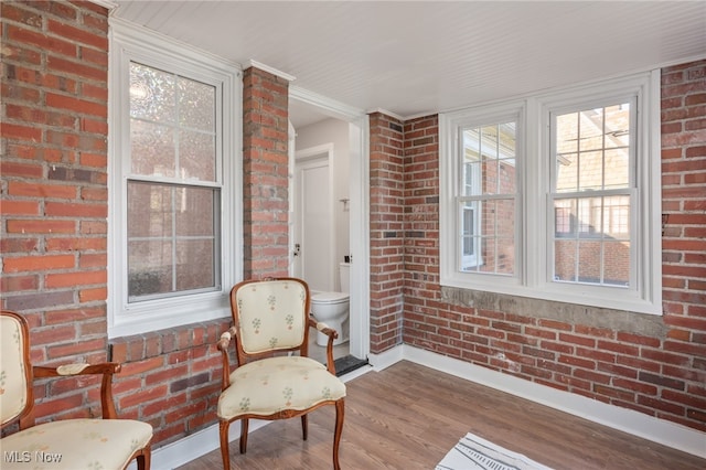 living area with brick wall and hardwood / wood-style flooring