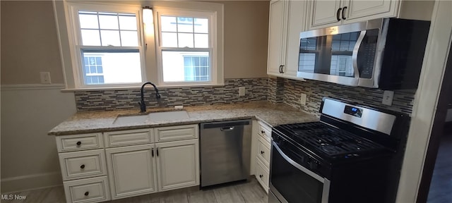 kitchen featuring white cabinets, sink, tasteful backsplash, light stone counters, and stainless steel appliances