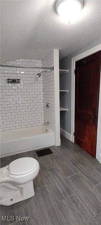 bathroom with tiled shower / bath, a textured ceiling, and toilet