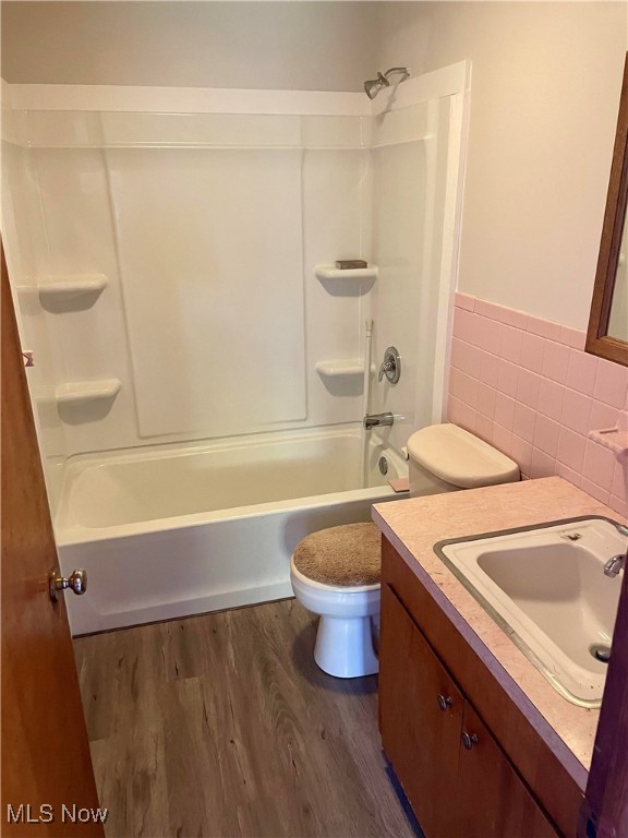 full bathroom with hardwood / wood-style flooring, toilet, shower / bathtub combination, vanity, and tile walls