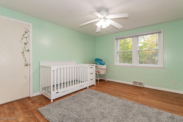 unfurnished bedroom with ceiling fan, a crib, and wood-type flooring