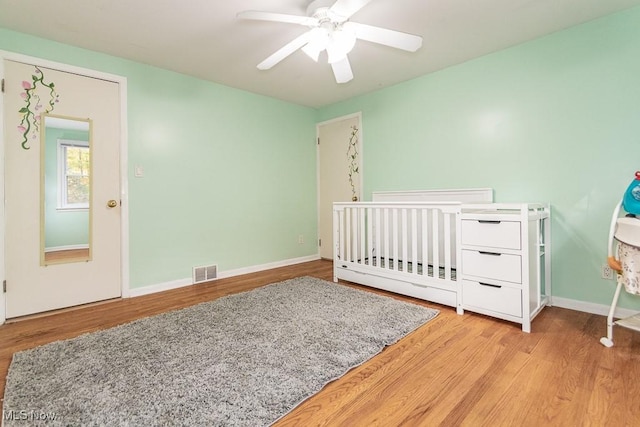 bedroom with ceiling fan, light hardwood / wood-style floors, and a crib