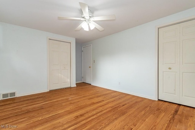 unfurnished bedroom featuring ceiling fan, light hardwood / wood-style floors, and multiple closets