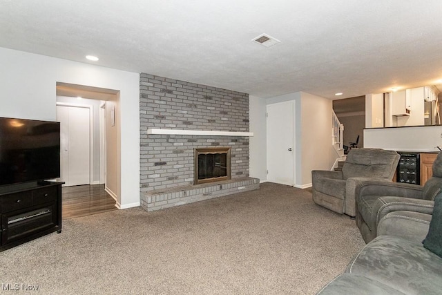 living room featuring wine cooler, carpet floors, a textured ceiling, and a brick fireplace